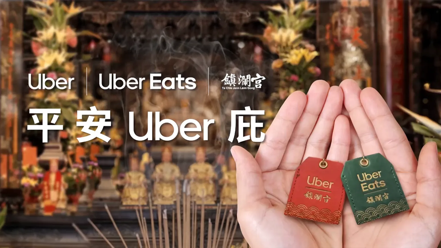 雙手捧著印有 Uber 與 Uber Eats 聯名鎮瀾宮的紅色與綠色平安符,背景為香火繚繞的廟宇神壇。